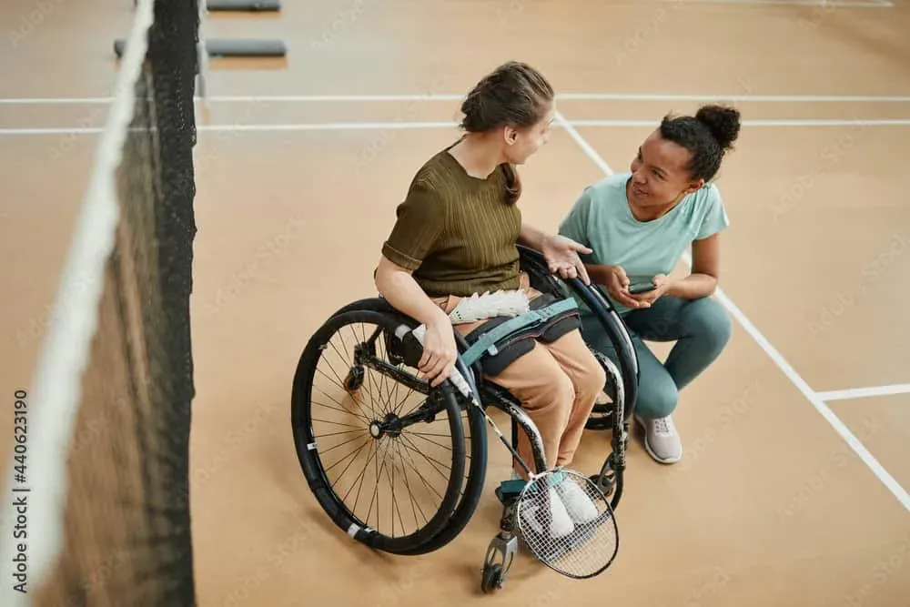 Zwei Frauen auf einem Badmintonplatz, eine von ihnen sitzt in einem Sportrollstuhl.